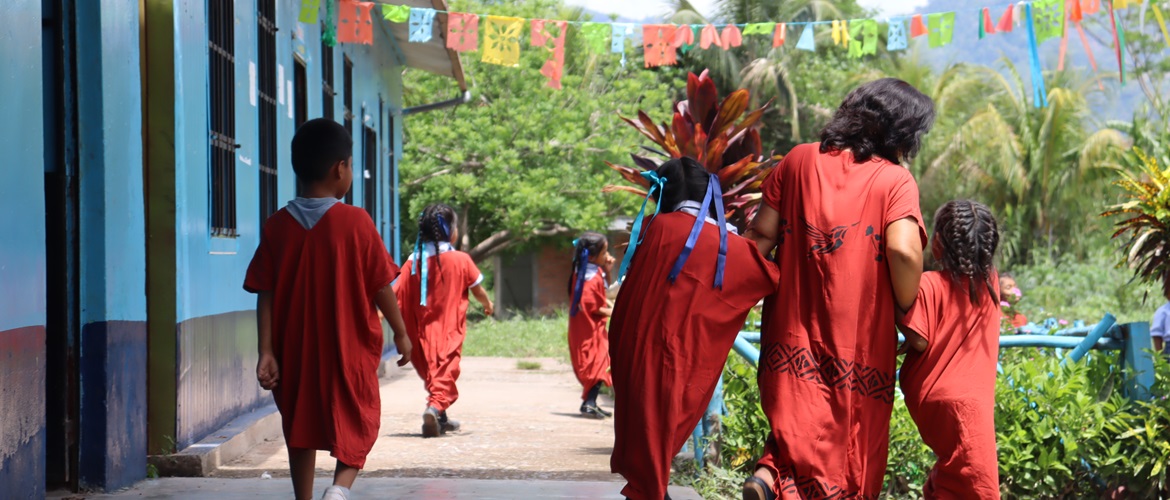 Woman, two girls and a boy all dressed in red walking along outside a blue painted school