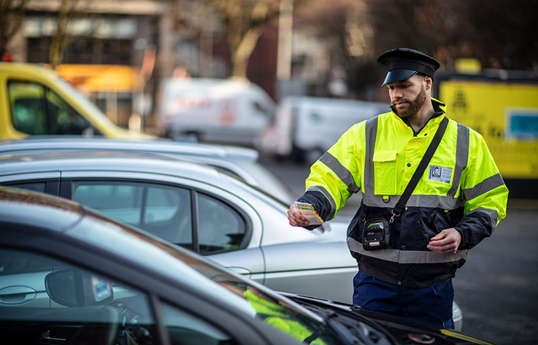 Eismo prižiūrėtojas padeda bilietą ant automobilio stovėjimo aikštelėje