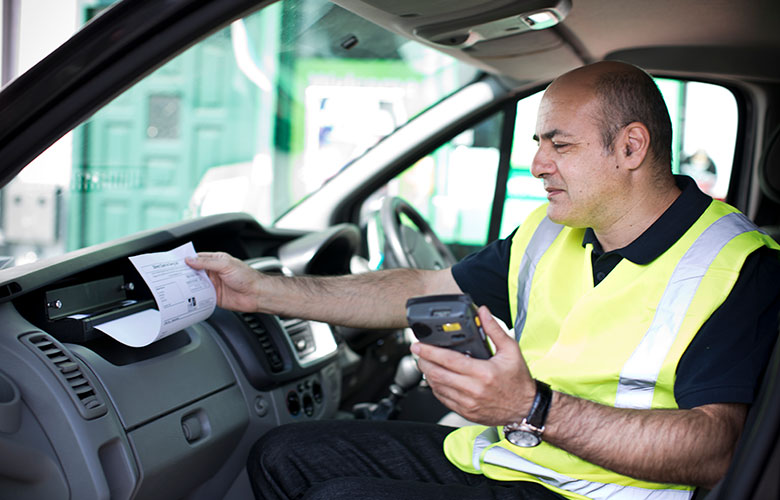 Gerai matomą liemenę vilkintis vyras transporto priemonės viduje spausdina A4 formato popieriaus lapą Brother PJ spausdintuvu