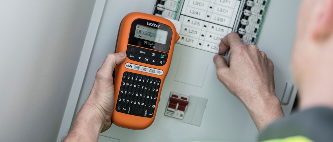 Elektrikas, laikantis mobilųjį etikečių spausdintuvą šalia saugiklių dėžutės