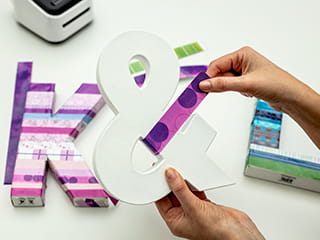 A woman is wrapping a full colour label printed on the Brother Design and Craft label printer, around a large ampersand character as part of her custom home decoration